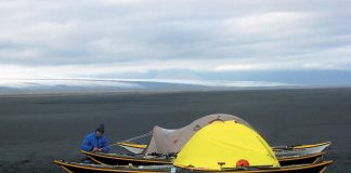 Person beside two black kayaks and a tent.