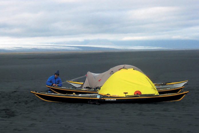 Person beside two black kayaks and a tent.