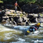 man standing on a rocky shelf above rapids lines a canoe without having to portage it