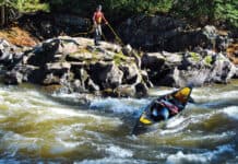 man standing on a rocky shelf above rapids lines a canoe without having to portage it