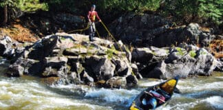 man standing on a rocky shelf above rapids lines a canoe without having to portage it
