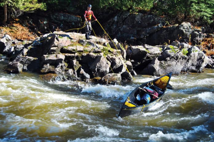 man standing on a rocky shelf above rapids lines a canoe without having to portage it