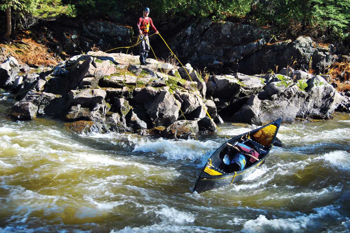 man standing on a rocky shelf above rapids lines a canoe without having to portage it