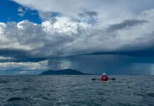 A sea kayaker sits on the water looking at a storm on the horizon