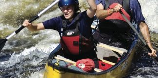 Two people paddle through whitewater in a Mad River Caption canoe