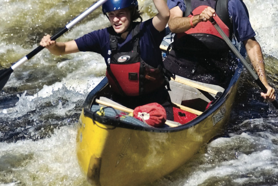 Two people paddle through whitewater in a Mad River Caption canoe