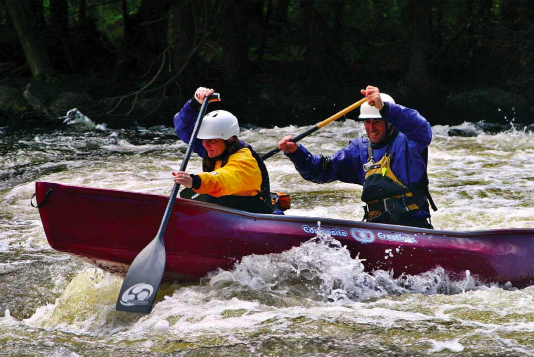Two people paddling a red canoe through whitewater.