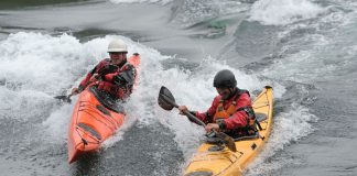Two men surf ocean waves in P&H Delphin kayaks