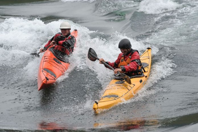 Two men surf ocean waves in P&H Delphin kayaks
