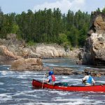 How To Solo & Tandem Back Ferry A Canoe Two people in a red canoe heading through swiftwater