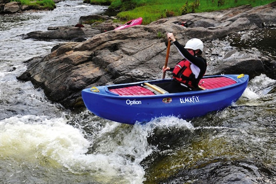 Person paddles the Blackfly Option canoe through a set of rapids