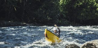 Woman paddling yellow canoe solo through rapids