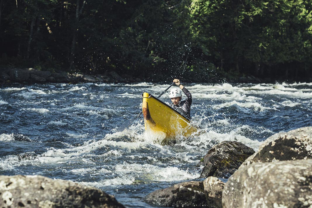 Woman paddling yellow canoe solo through rapids