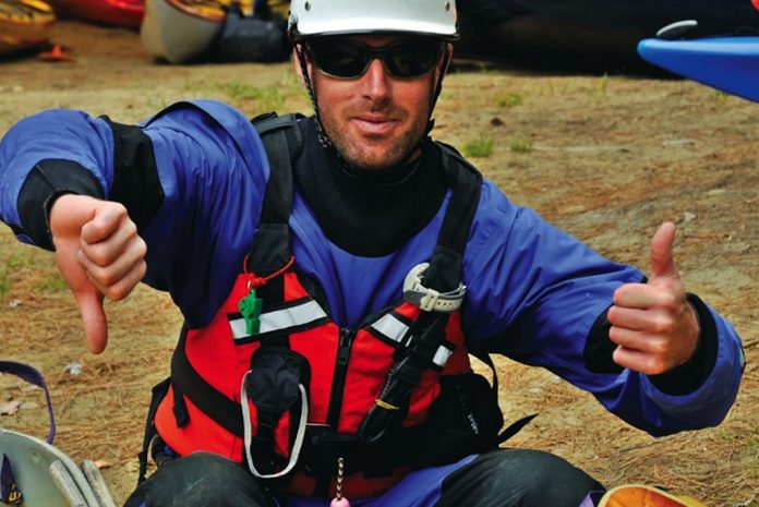 Male paddler sits in front of two canoes giving thumbs-up and thumbs-down hand signals.