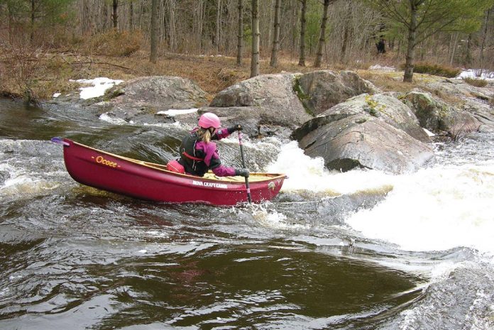 Woman paddling open boat down a rapid