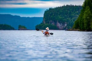 woman paddling away from the camera along a rocky, wild shore