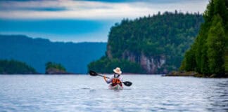 woman paddling away from the camera along a rocky, wild shore