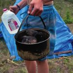 6 Steps For Building A DIY Backcountry Sauna Person holding a jug of water and pot with blue tarp in background
