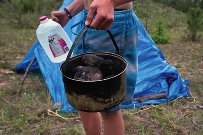 Person holding a jug of water and pot with blue tarp in background