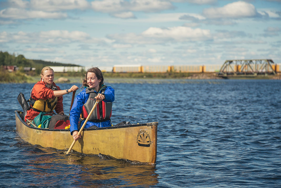 Two people canoeing on a windy day, train bridge in background