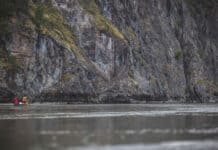 people paddle a canoe in front of a large grey rock face