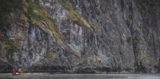 people paddle a canoe in front of a large grey rock face