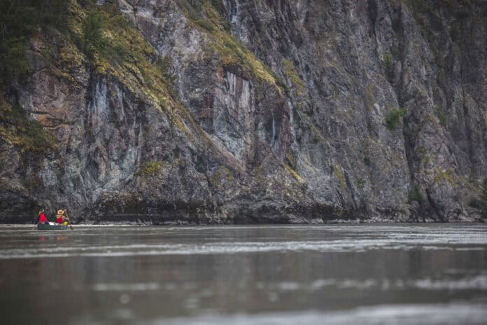 people paddle a canoe in front of a large grey rock face