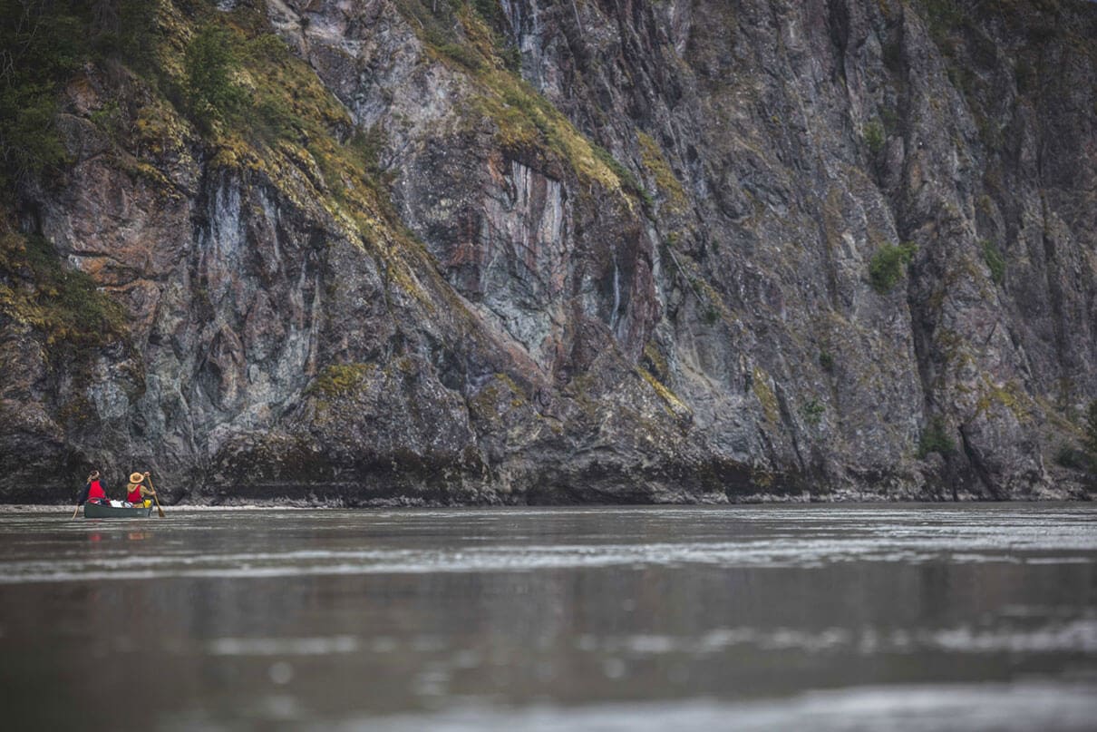 people paddle a canoe in front of a large grey rock face