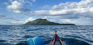 bow shot of a sea kayak paddling in a straight line across open water to the dramatic Sleeping Giant