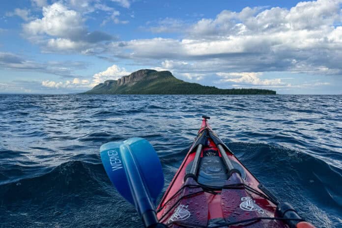 bow shot of a sea kayak paddling in a straight line across open water to the dramatic Sleeping Giant