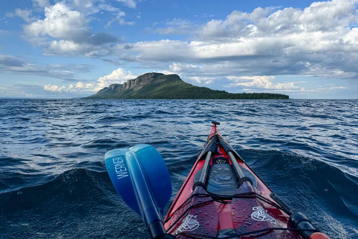 bow shot of a sea kayak paddling in a straight line across open water to the dramatic Sleeping Giant