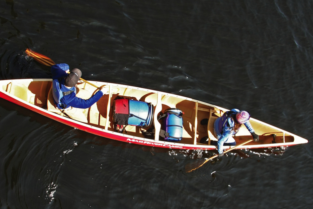 Overhead view of two people in red canoe with blue barrels