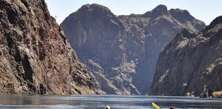 Two kayakers on river with volcanic cliffs in background