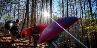Three people carrying whitewater kayaks through the woods