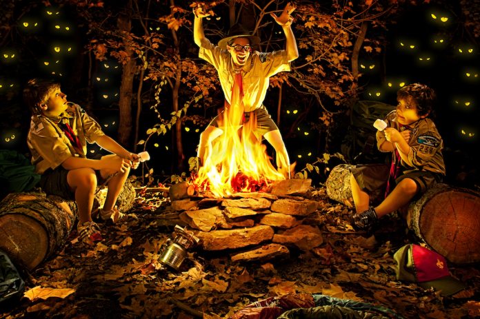 Camp councillor telling scary stories and camping myths to two boy scouts around the fire