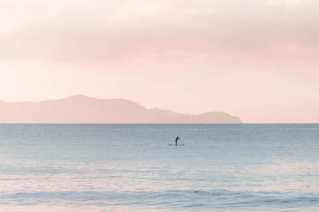 a person standing on a SUP and paddling in front of pinkish skies and silhouetted hills
