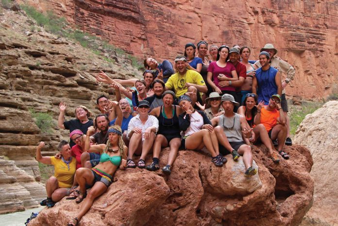 Group of people sitting on a boulder by a river.