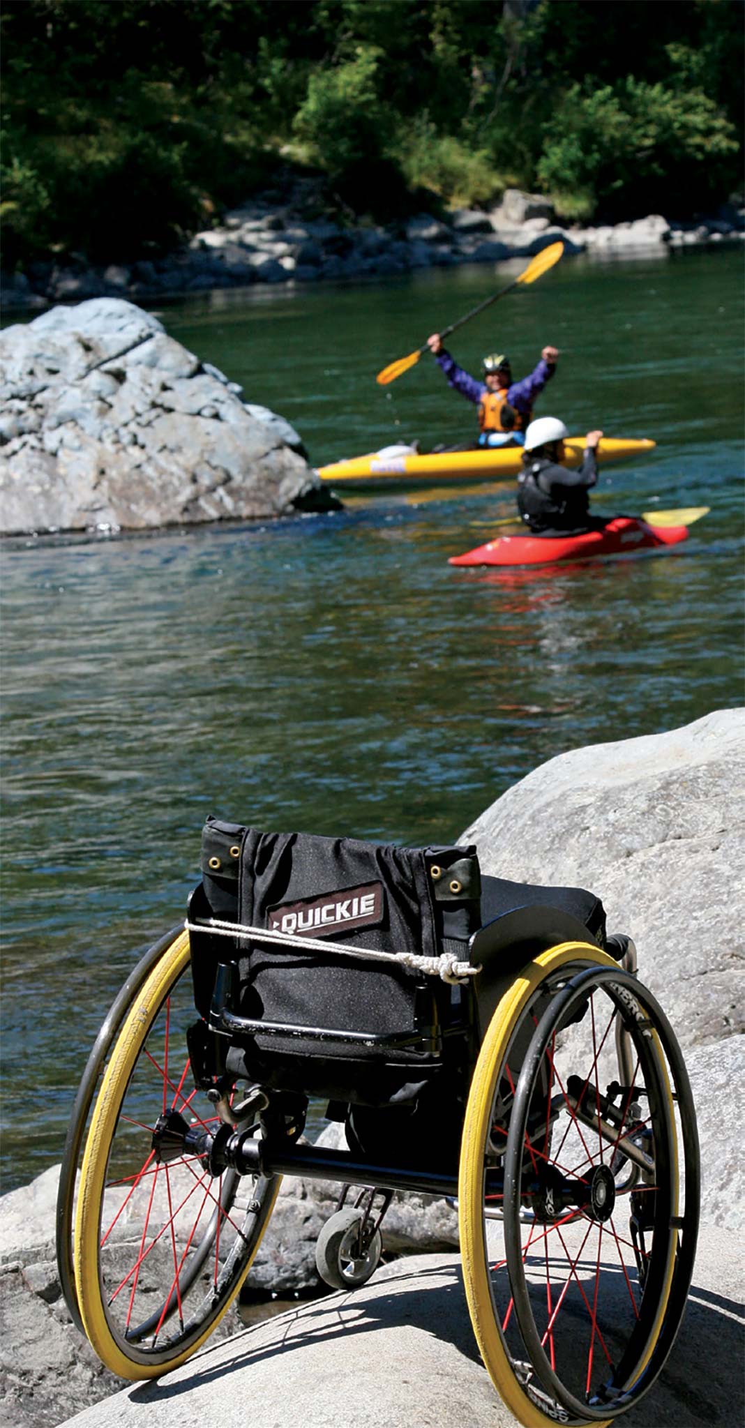 Wheelchair in foreground with two kayakers on river in background