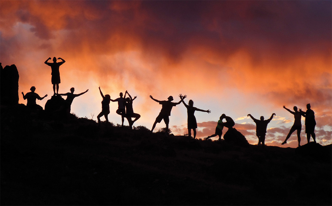 People standing on hill silhouetted with sunset in background