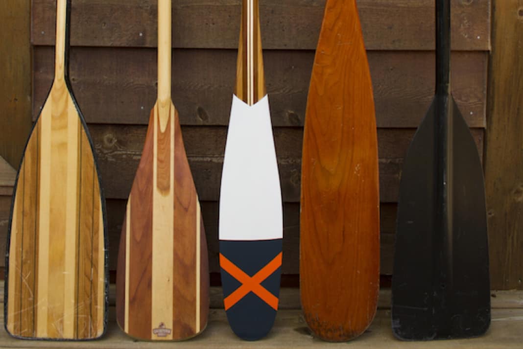 Five canoe paddles lined up along wall
