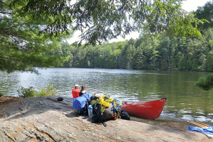 Two people sitting on the shore with canoe and packs pulled up beside.