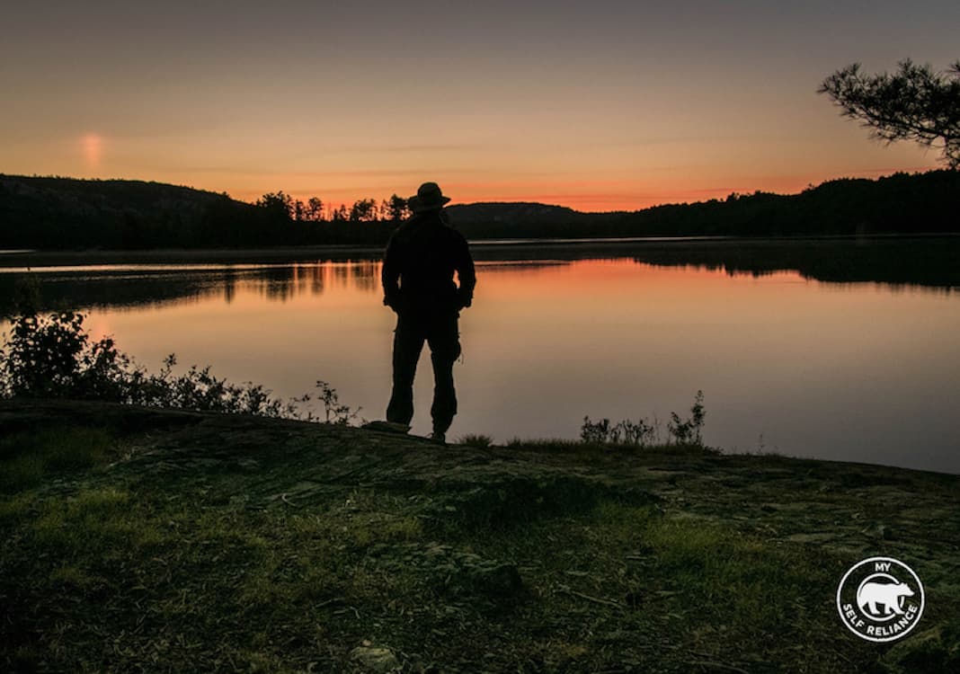 Shawn James stands in front of a sunset on a solo canoe trip