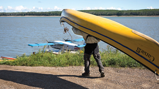 Person portaging yellow canoe beside floatplane