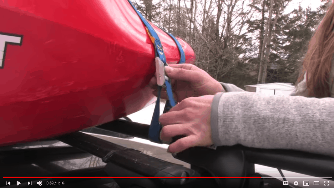 Someone adjusting straps around kayak on roof of car.