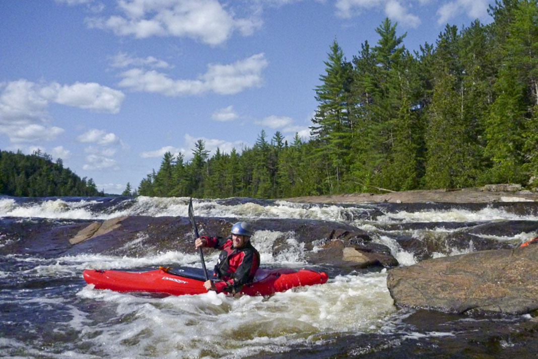 A whitewater kayaker at the base of a rapid in a red creek boat.