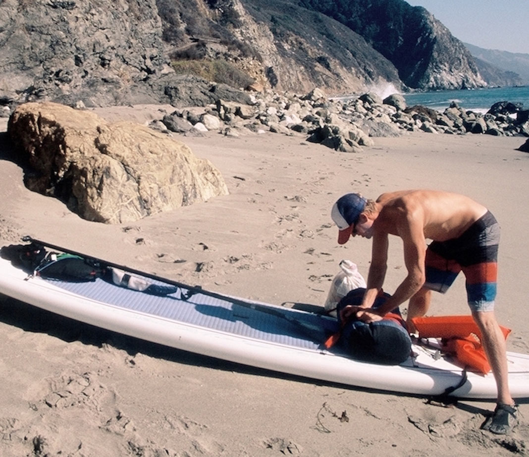 Man strapping things to his paddleboard on the beach