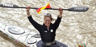 Woman in sea kayak raising paddle above her head.