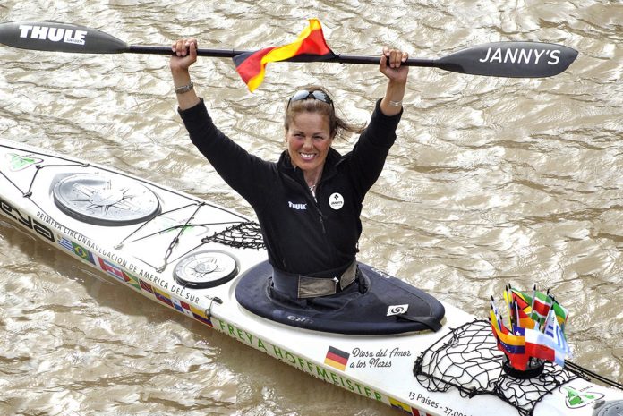 Woman in sea kayak raising paddle above her head.