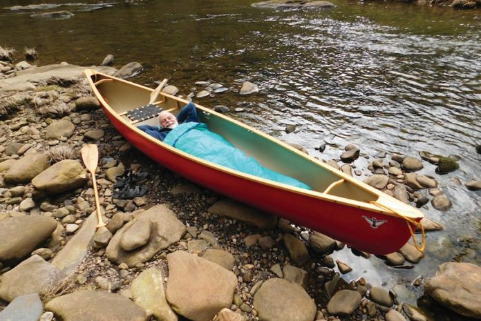 Man lying in a canoe pulled up on shore.
