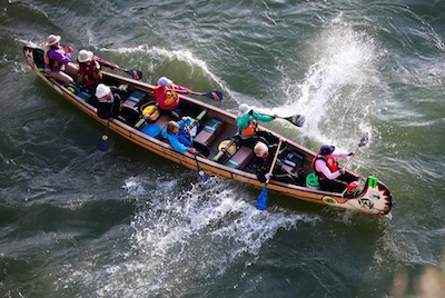 A group of people paddle in a large racing canoe